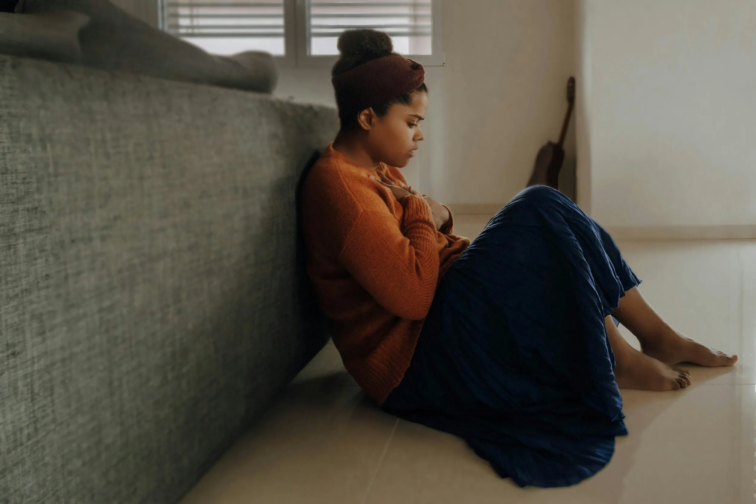 A person sitting on the floor against a sofa, with their knees drawn up.