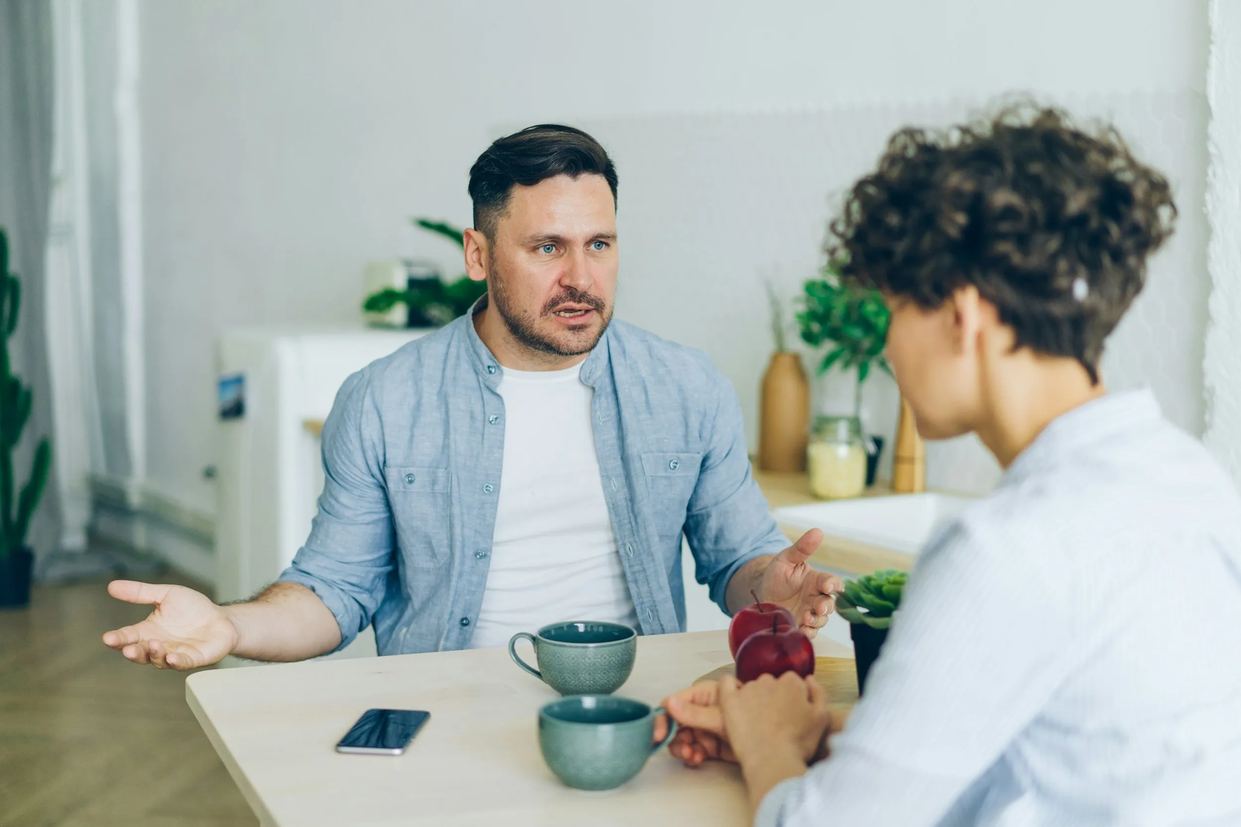 Two people talking across a table, with one gesturing with open hands.